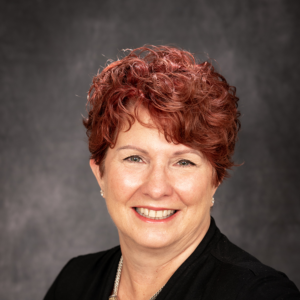 A woman with red hair and black jacket smiling.